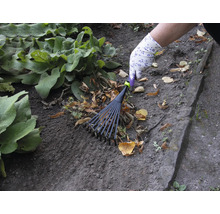 En person räfsar löv med en lövräfsa i trädgården.