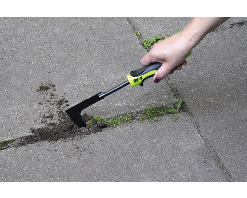 En hand använder en fogskrapa för att ta bort ogräs mellan gatstenar.