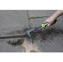 En person tar bort ogräs med en fogskrapa på en stenlagd yta.