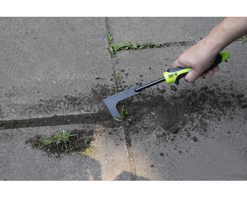 En person tar bort ogräs med en fogskrapa på en stenlagd yta.