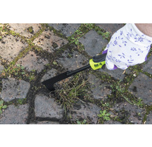 Person tar bort ogräs mellan gatstenar med en fogskrapa från for_q.