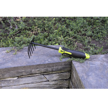 Löv- och trädgårdsräfsa med pinnar och plasthandtag på stenmur