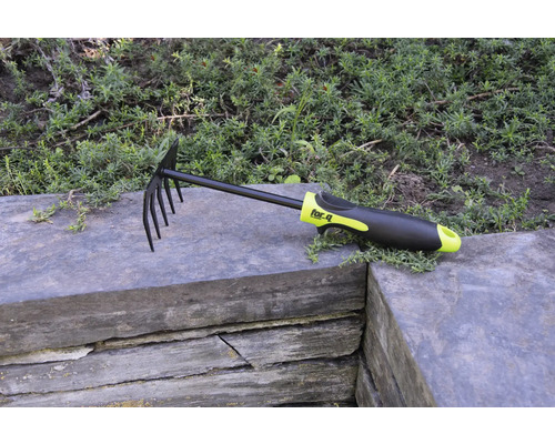 Löv- och trädgårdsräfsa med pinnar och plasthandtag på stenmur