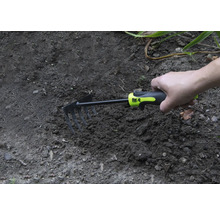 Hand håller en liten kratta i trädgårdsjorden