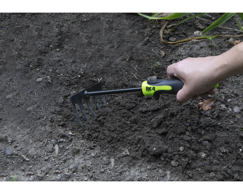 Hand håller en liten kratta i trädgårdsjorden