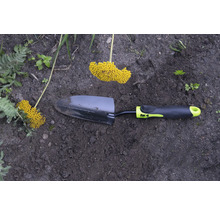 Trädgårdsspade med gult blomställ i trädgårdsrabatten