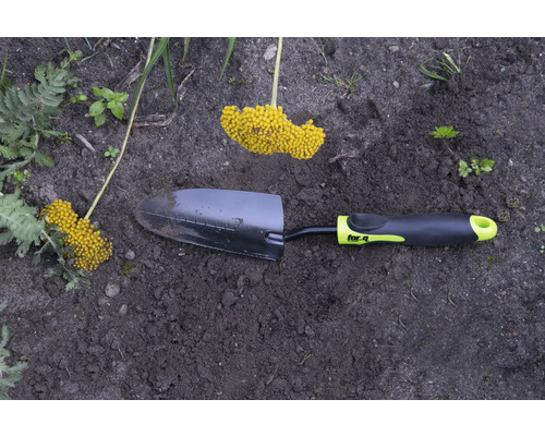 Trädgårdsspade med gult blomställ i trädgårdsrabatten