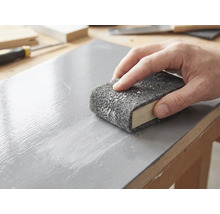 En hand slipar en lackerad träyta med en slipvlies som är lindad runt ett slipblock.