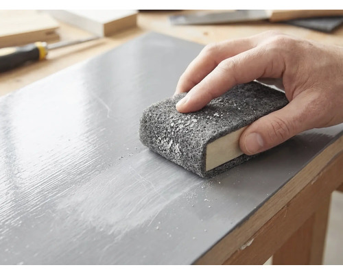 En hand slipar en lackerad träyta med en slipvlies som är lindad runt ett slipblock.