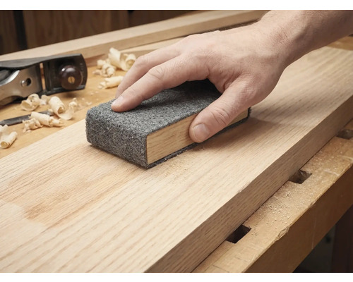 Hand som slipar en träplanka med en slipduk på en slipkloss.