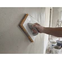 Hand som drar ett svampbräde över en putsad vägg.