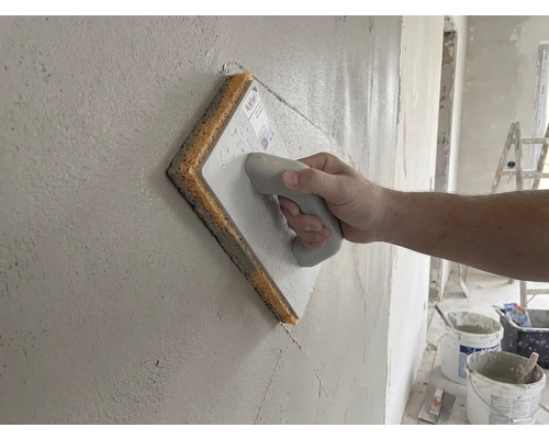 Hand som drar ett svampbräde över en putsad vägg.