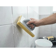 En person rengör nyligen fogat väggkakel med en svampbräda och vatten.