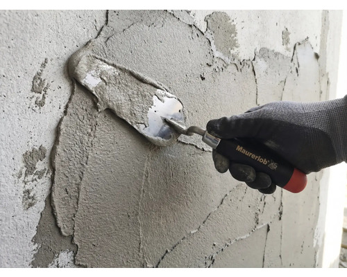 En hand med arbetshandske applicerar murbruk på en vägg med en murarslev från Maurerlob.