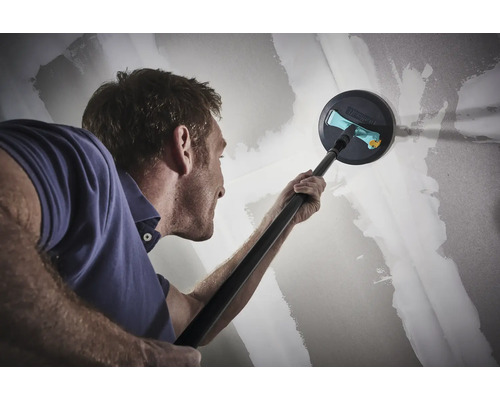 En man slipar en gipsvägg med en giraffslipmaskin.