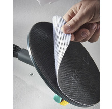 En hand fäster en vit nätsliprondell på den svarta runda slipplattan på en väggslipmaskin.