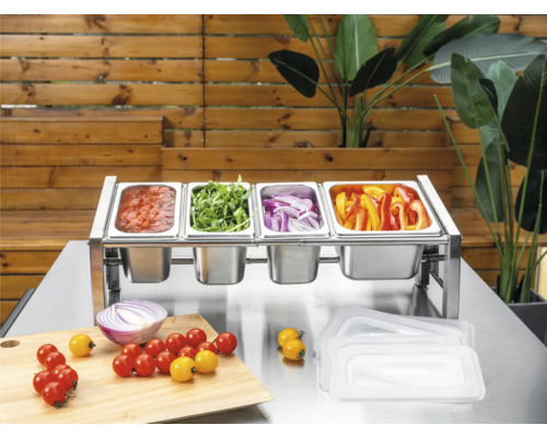 Ingrediensstation i rostfritt stål med fyra Gastronorm-kantiner fyllda med grönsaker och sås på ett metallbord med skärbräda.