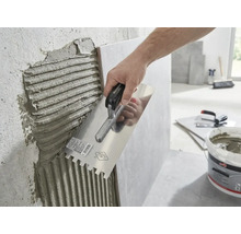 En hand applicerar fästmassa på en vägg med en tandspackel.