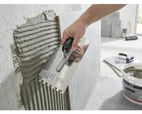 En hand applicerar fästmassa på en vägg med en tandspackel.