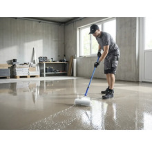 En man använder en piggroller med teleskopskaft för att avlufta en nylagd golvavjämningsmassa i ett ljust rum.