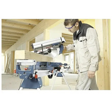 Hantverkare sågar en träbalk med en Bosch kap- och gersåg monterad på ett stativ i en ljus byggmiljö.