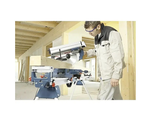 Hantverkare sågar en träbalk med en Bosch kap- och gersåg monterad på ett stativ i en ljus byggmiljö.