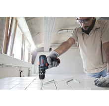 Person som använder en sladdlös slagborrmaskin från Bosch för att borra i vita kakelplattor på en byggarbetsplats.