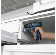 Bosch Professional sladdlös borrskruvdragare vid montering av lådskenor av metall i ett vitt skåp.