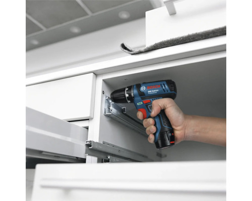 Bosch Professional sladdlös borrskruvdragare vid montering av lådskenor av metall i ett vitt skåp.