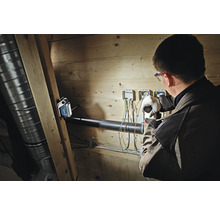 En batteridriven arbetslampa från Bosch lyser upp en hantverkare vid elarbeten på en trävägg.