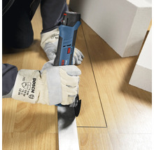 Person med skyddshandskar skär en rät linje i ett trägolv med ett Bosch Professional batteridrivet multiverktyg.