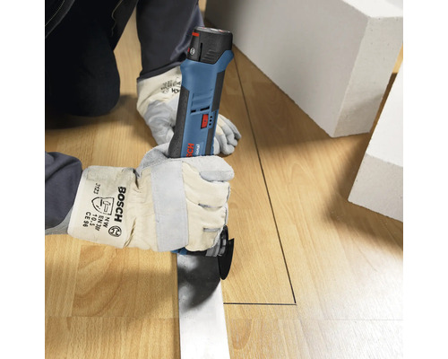 Person med skyddshandskar skär en rät linje i ett trägolv med ett Bosch Professional batteridrivet multiverktyg.