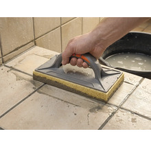 En svampbräda används för att rengöra nyligen fogat kakel. En hand för brädan över de blöta plattorna.