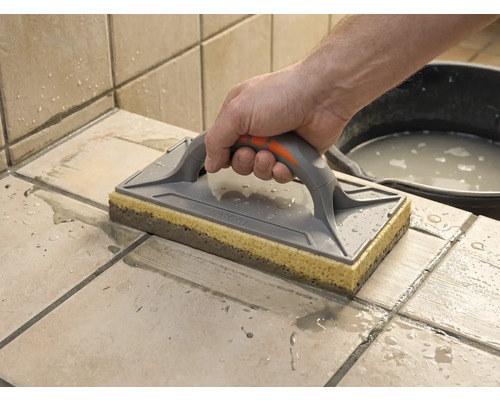 En svampbräda används för att rengöra nyligen fogat kakel. En hand för brädan över de blöta plattorna.