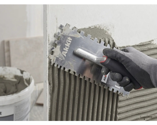 En hand med handske applicerar fästmassa jämnt på en vägg med en Akkit fixkam.