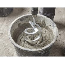 En spiralomrörare blandar grått bruk i en svart bygghink.