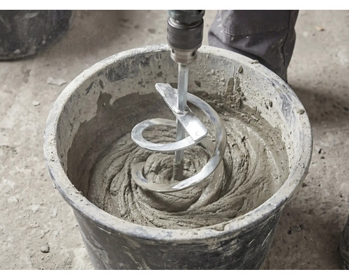 En spiralomrörare blandar grått bruk i en svart bygghink.