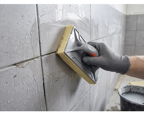 En hand rengör nyligen fogat kakel med en svampbräda och vatten.