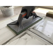 Hand med arbetshandske som använder en fogbräda för att foga kakelplattor.