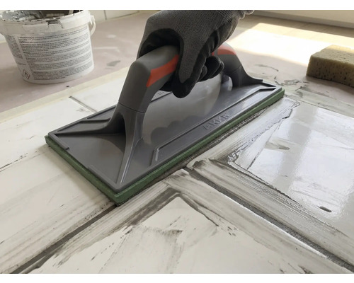 Hand med arbetshandske som använder en fogbräda för att foga kakelplattor.