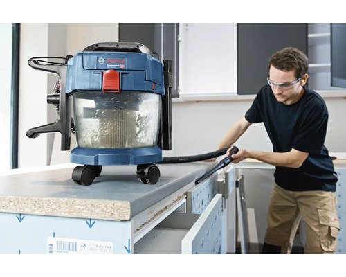 Bosch batteridriven våt- och torrdammsugare som används för att rengöra en arbetsbänk i en ljus verkstad.