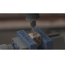 Dremel rotationsverktyg borrar hål i en trätärning som sitter fast i ett Dremel-skruvstycke.