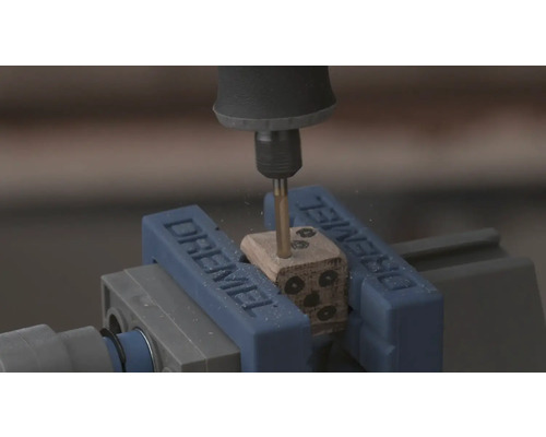 Dremel rotationsverktyg borrar hål i en trätärning som sitter fast i ett Dremel-skruvstycke.