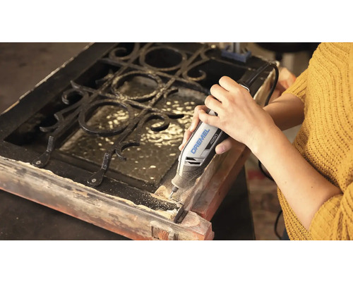 En person använder ett Dremel 4250 multiverktyg för att bearbeta en träram med metallgaller.