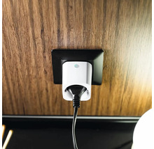 Vit smart kontakt med svart kabel i ett svart eluttag på en vägg med trästruktur.