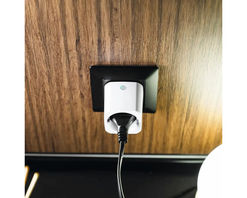Vit smart kontakt med svart kabel i ett svart eluttag på en vägg med trästruktur.