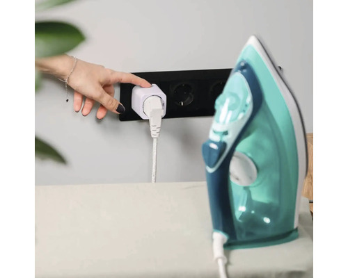 En hand trycker på knappen på en vit smart kontakt i ett svart vägguttag, ansluten till ett strykjärn.