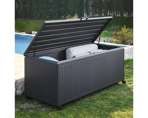 Mörkgrå trädgårdsdyna i metall med öppet lock och hjul, fylld med kuddar, bredvid en pool i trädgården.