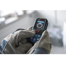 Bosch Professional laseravståndsmätare som används av händer i arbetshandskar, digital display med mätfunktioner.