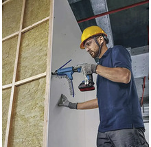 Yrkesman monterar gipsskivor på en isolerad trävägg med en batteridriven gipsskruvdragare med magasin.